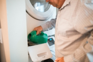 Man pouring laundry detergent out of a green bottle into a washing machine