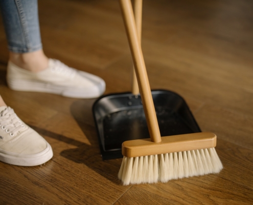 Person in white shoes and jeans using a broom and dustpan