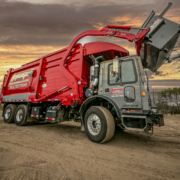 a red garbage truck is parked on a dirt road