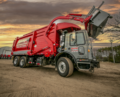 a red garbage truck is parked on a dirt road